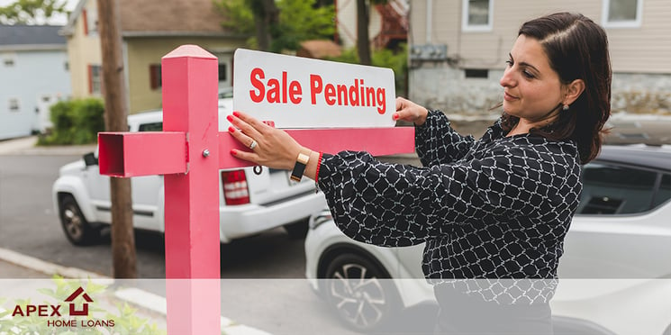 A realtor displaying a sign that says "sale pending" in front of a home. 